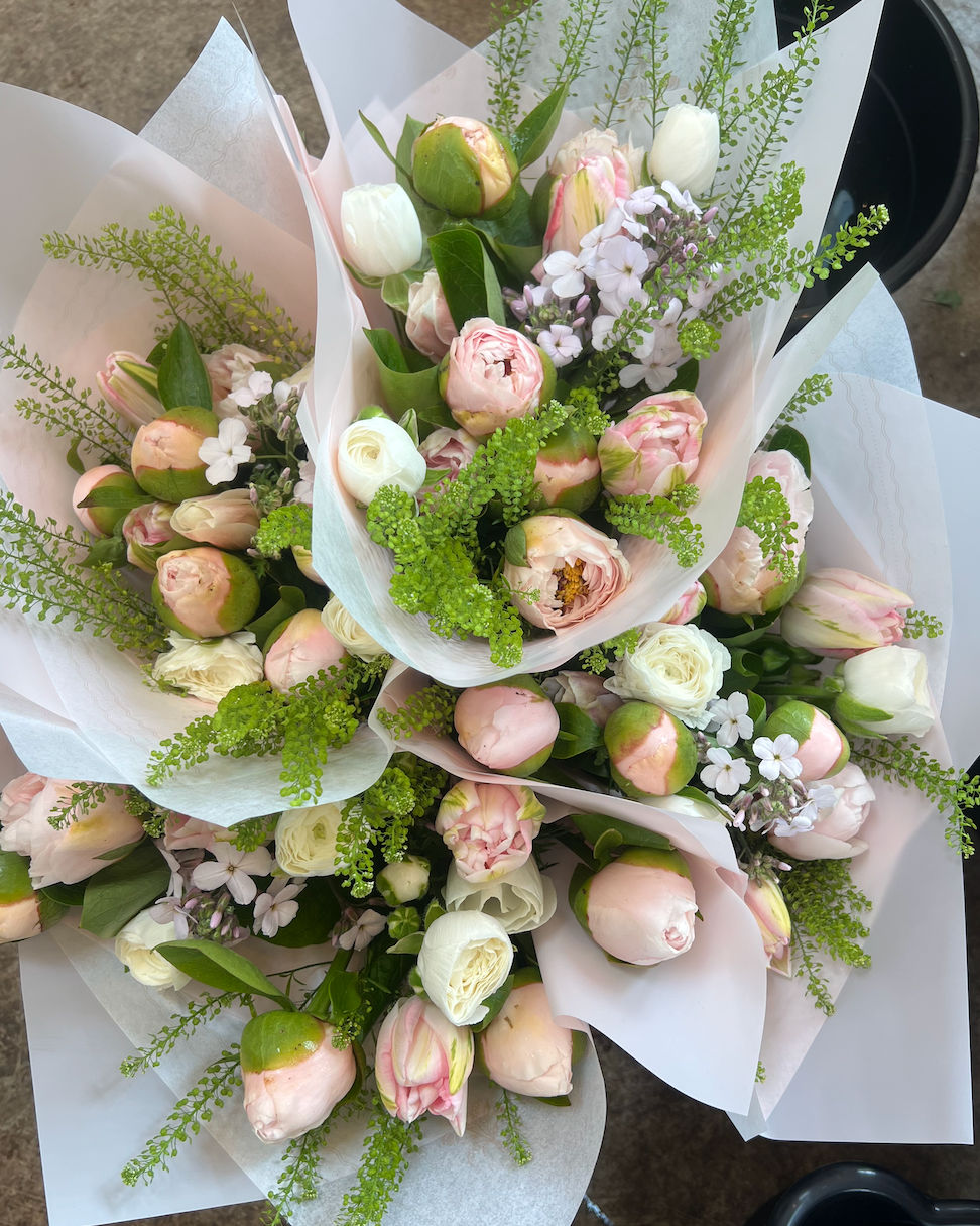 Three bouquets of flowers wrapped in white paper on a dark surface