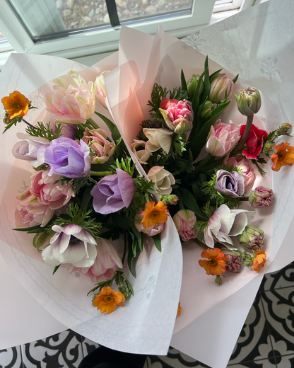 Two bouquets of flowers on a table with a window in the background