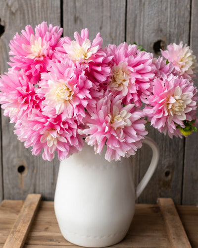 White vase with pink flowers on a wooden surface against a rustic wooden background
