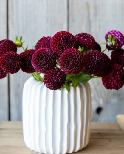 White vase with purple flowers on a wooden surface and light wooden panel background