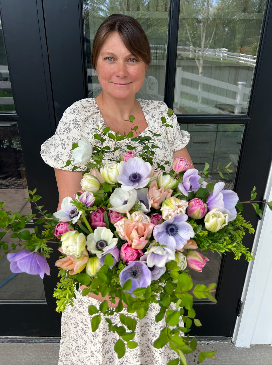 Woman holding a large bouquet of flowers in front of a glass door.