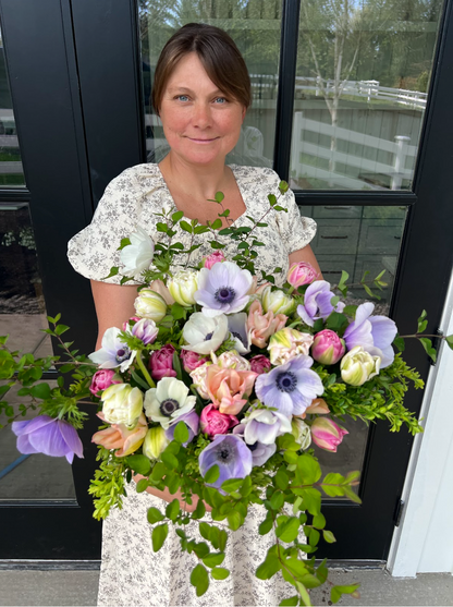 Woman holding a large bouquet of flowers in front of a glass door.