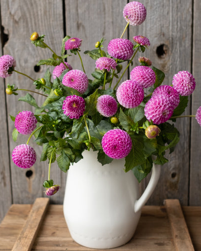 Bouquet of pink flowers in a white vase on a wooden surface with a rustic wooden background.