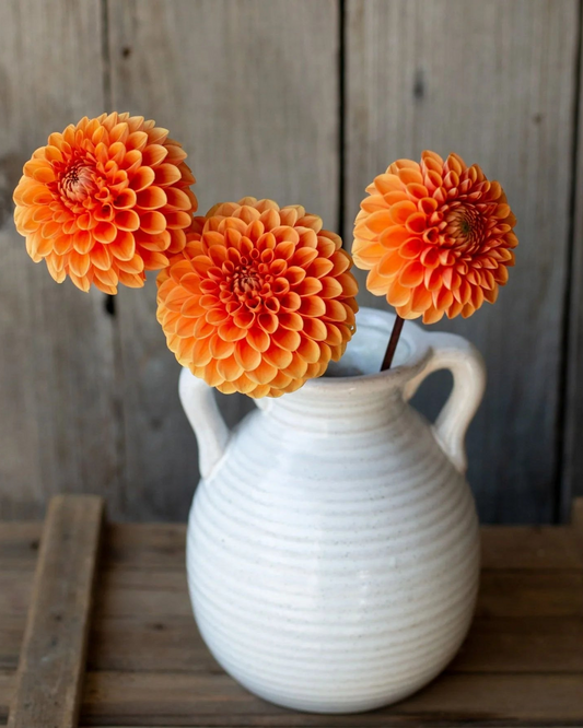 White ceramic pitcher with orange flowers against a wooden background