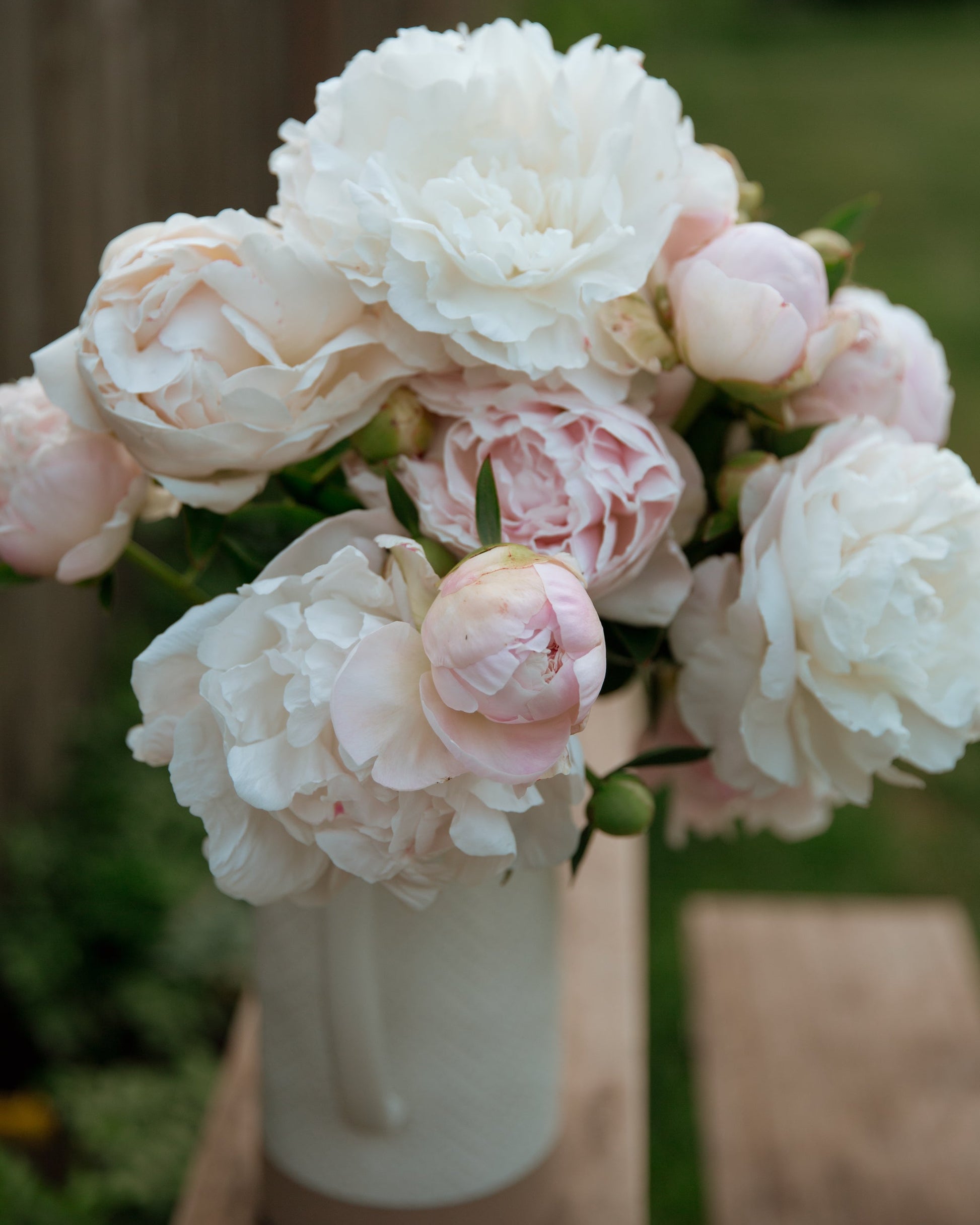 Bouquet of white and pink flowers in a vase on a wooden surface with a blurred natural background