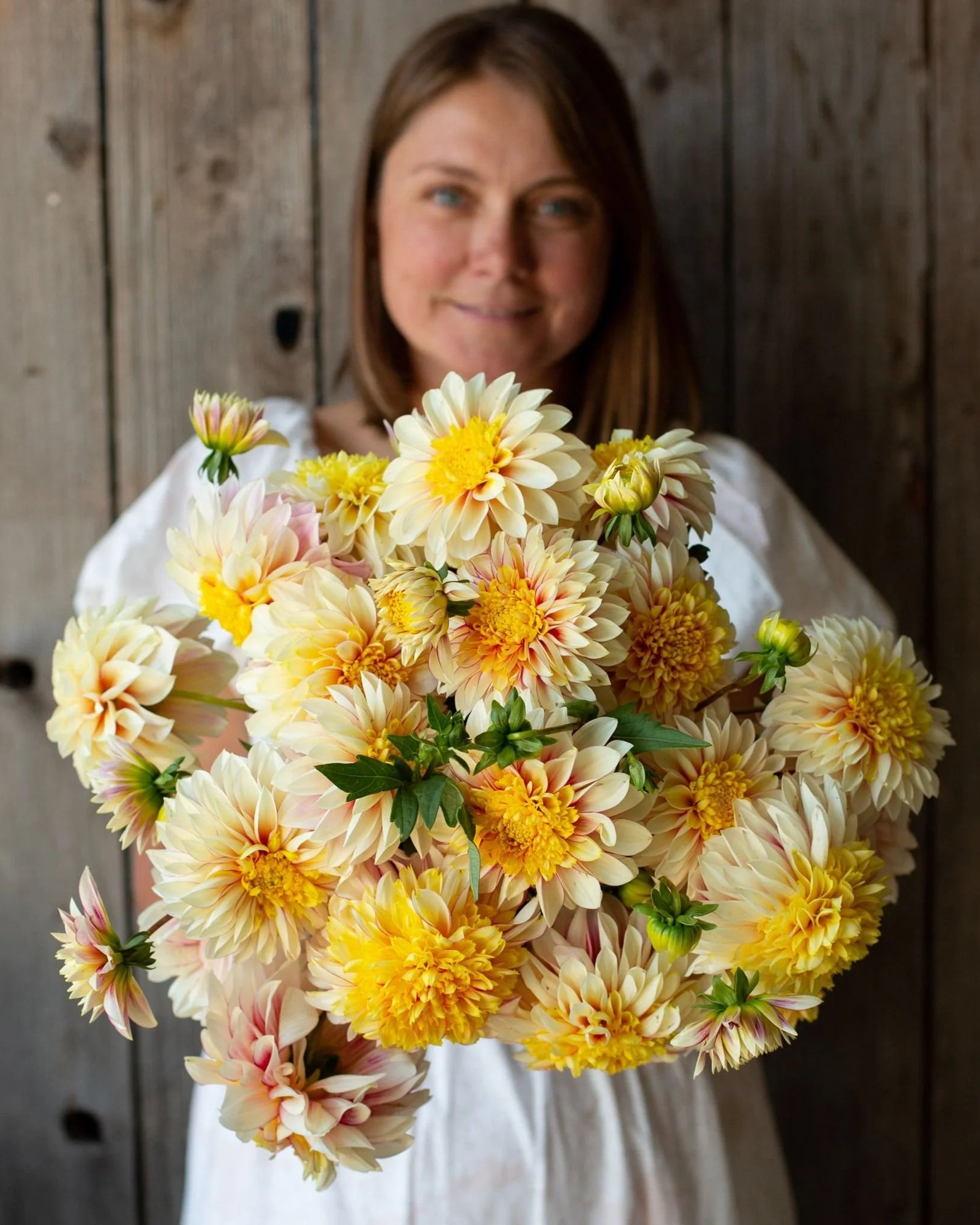 Woman holding a large bouquet of yellow and white flowers against a wooden background
